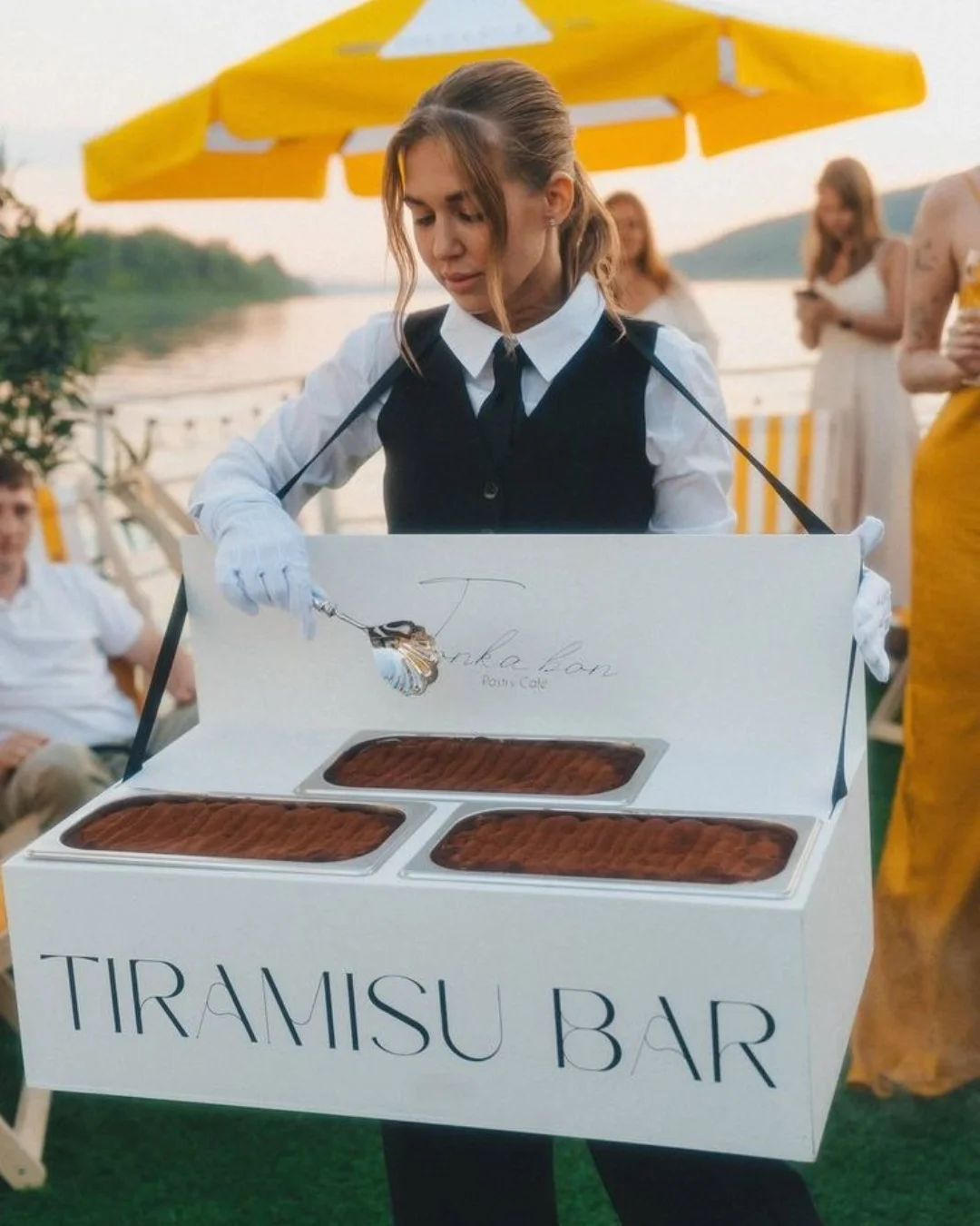 A server at an outdoor tiramisu bar under a yellow parasol